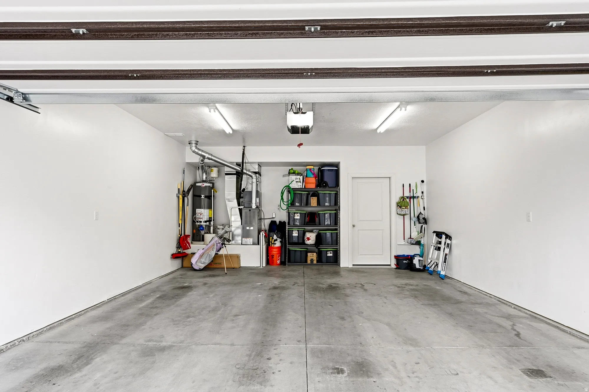 Concrete flooring garage with white painted walls, overhead fluorescent lighting, and a built-in water heater