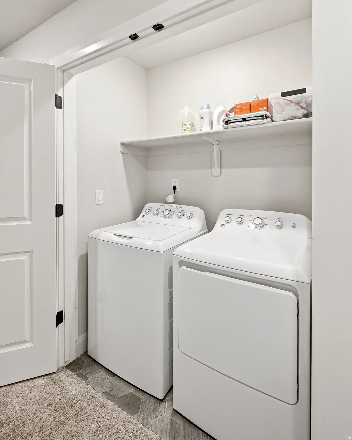 Dedicated laundry area with a white built-in shelf, hexagonal tile flooring, and a white paneled door with black hardware