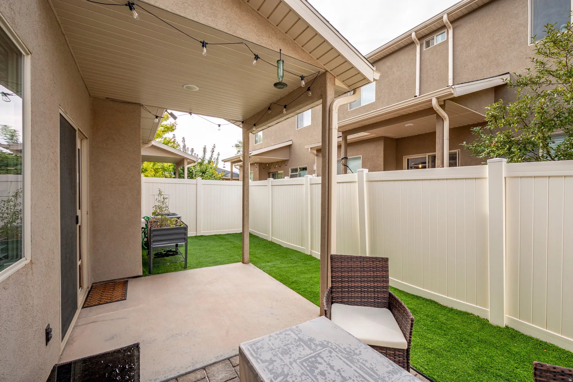 Covered patio with concrete flooring, artificial turf, and privacy fencing