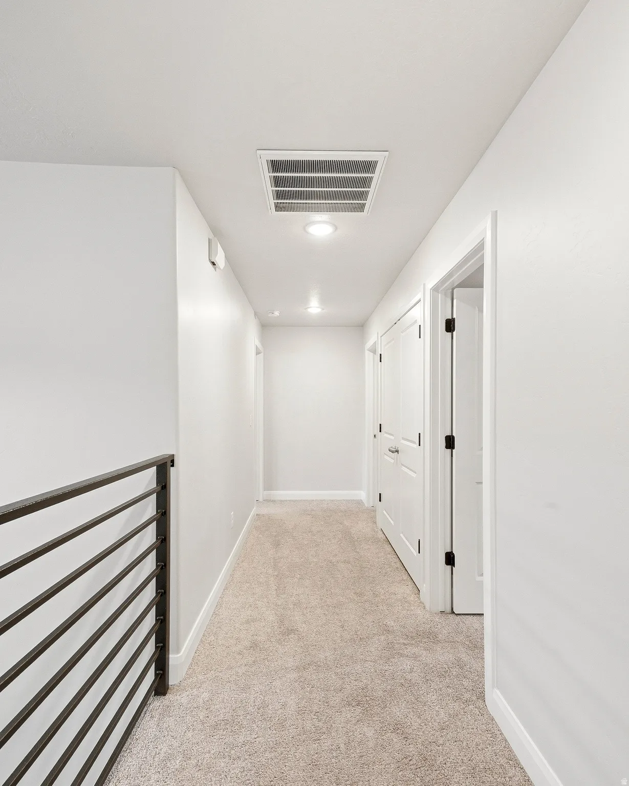 Hallway with light-toned carpeting, recessed lighting, and a contemporary metal railing