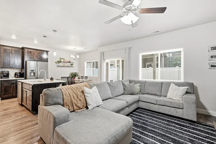 Open-concept living area featuring a ceiling fan, wood-finish flooring, and ample natural light from multiple windows