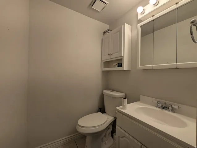 White vanity with integrated sink, chrome faucet, medicine cabinet with mirrored doors, wall-mounted light fixture, and white wall-mounted cabinet