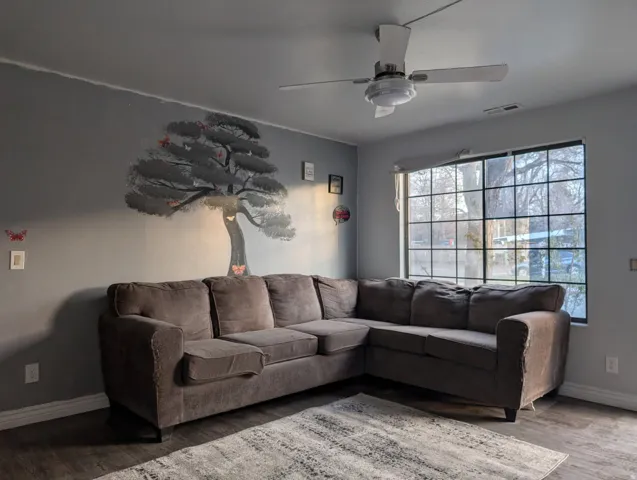 Wall-mounted ceiling fan, large grid-pattern window, wood-finish flooring, and painted wall mural