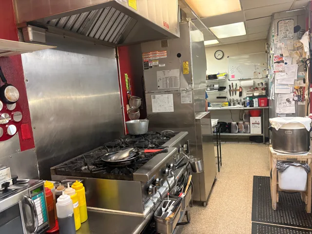 Commercial kitchen featuring a stainless steel range with multiple burners, a large stainless steel hood, and a stainless steel backsplash