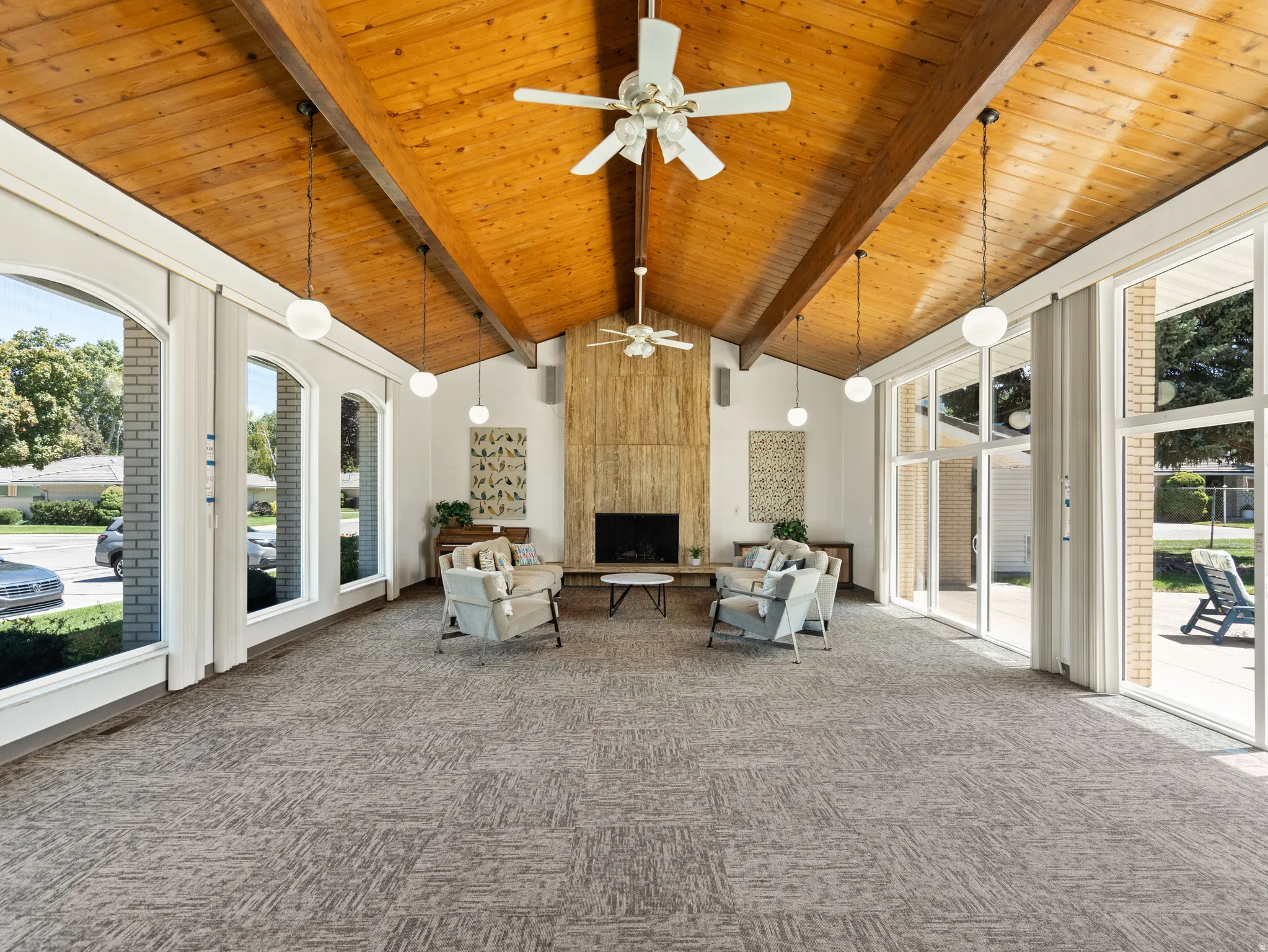 Vaulted wood-finish ceiling with exposed beams, full-height stone-clad fireplace, expansive windows, and glass sliding doors