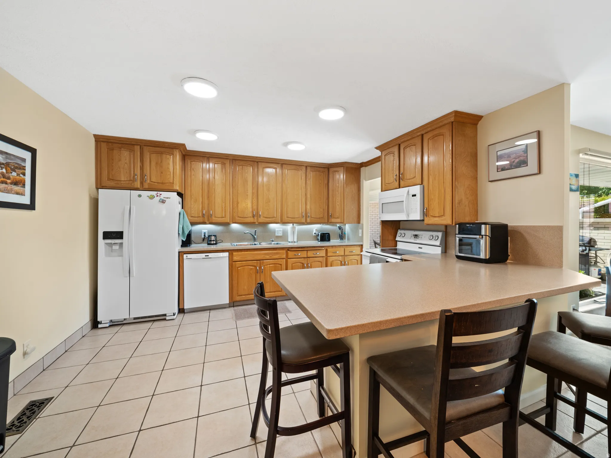 Kitchen featuring light-finish cabinetry, white appliances, recessed lighting, and a breakfast bar with solid surface countertop