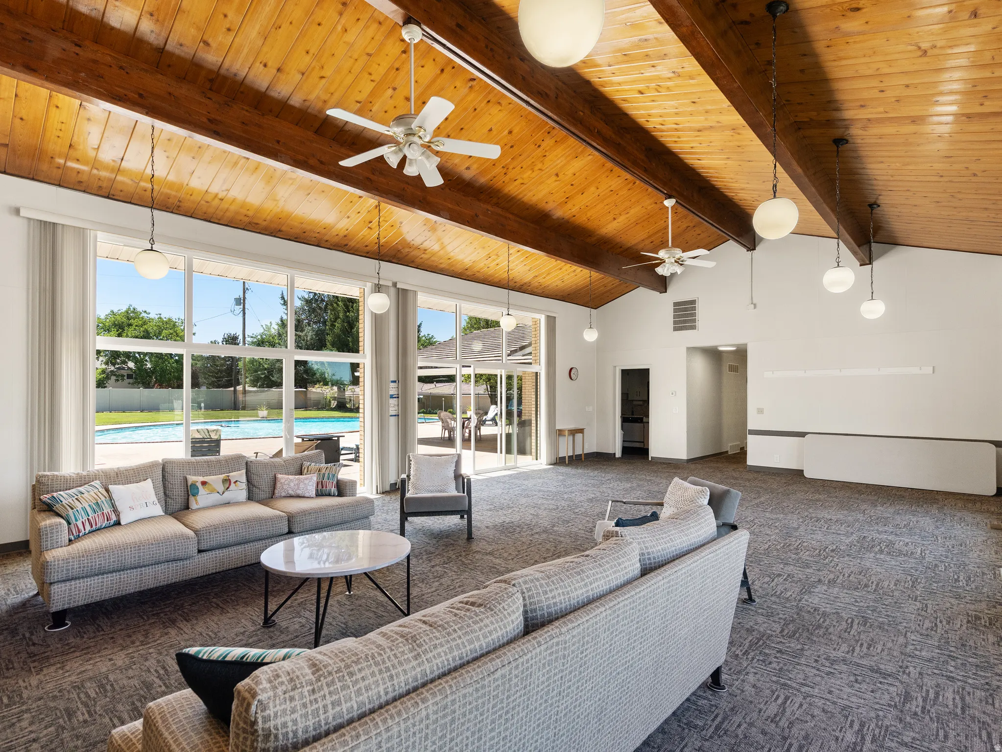 Vaulted wood-finish ceilings with exposed beams, multiple ceiling fans, and large picture windows