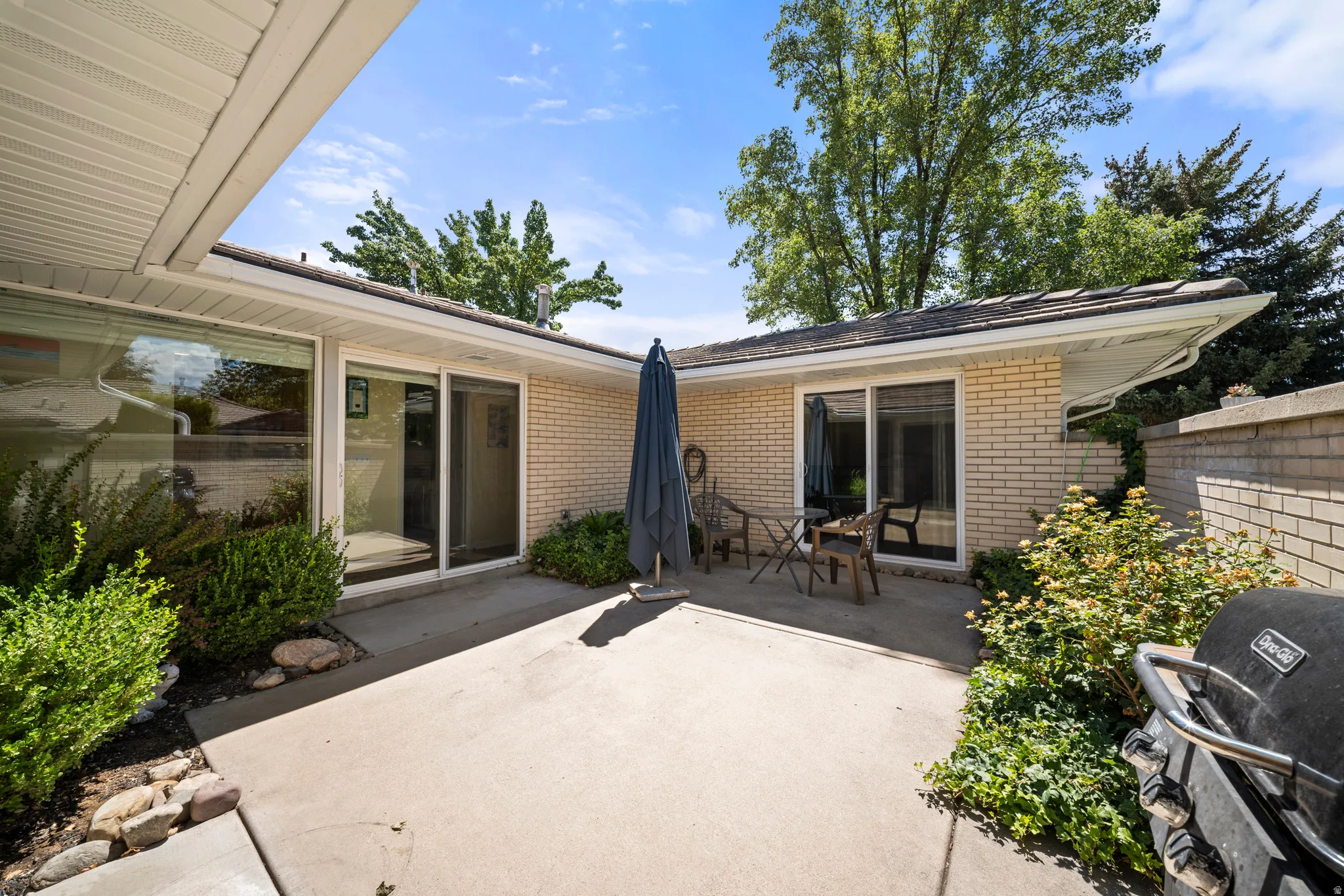Concrete patio with a brick exterior, multiple large windows, and a shingle roof