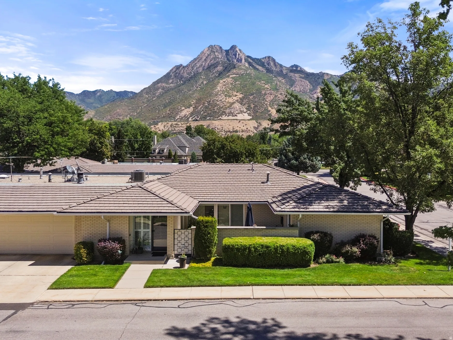 Mountain backdrop, a tile roof, an attached garage, a concrete driveway, and mature landscaping