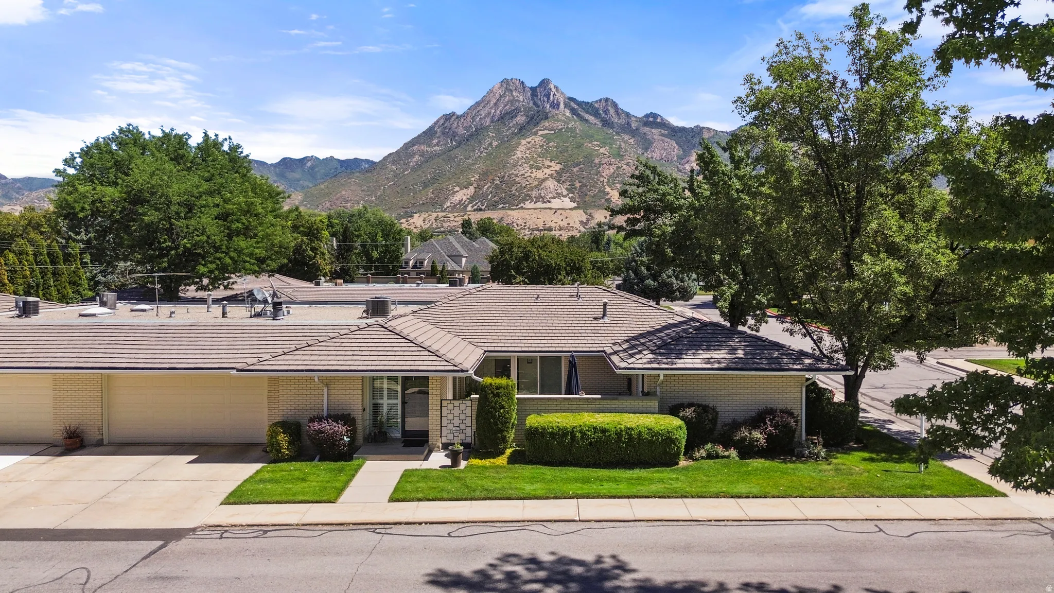 Mountain backdrop, a tile roof, an attached garage, a concrete driveway, and mature landscaping