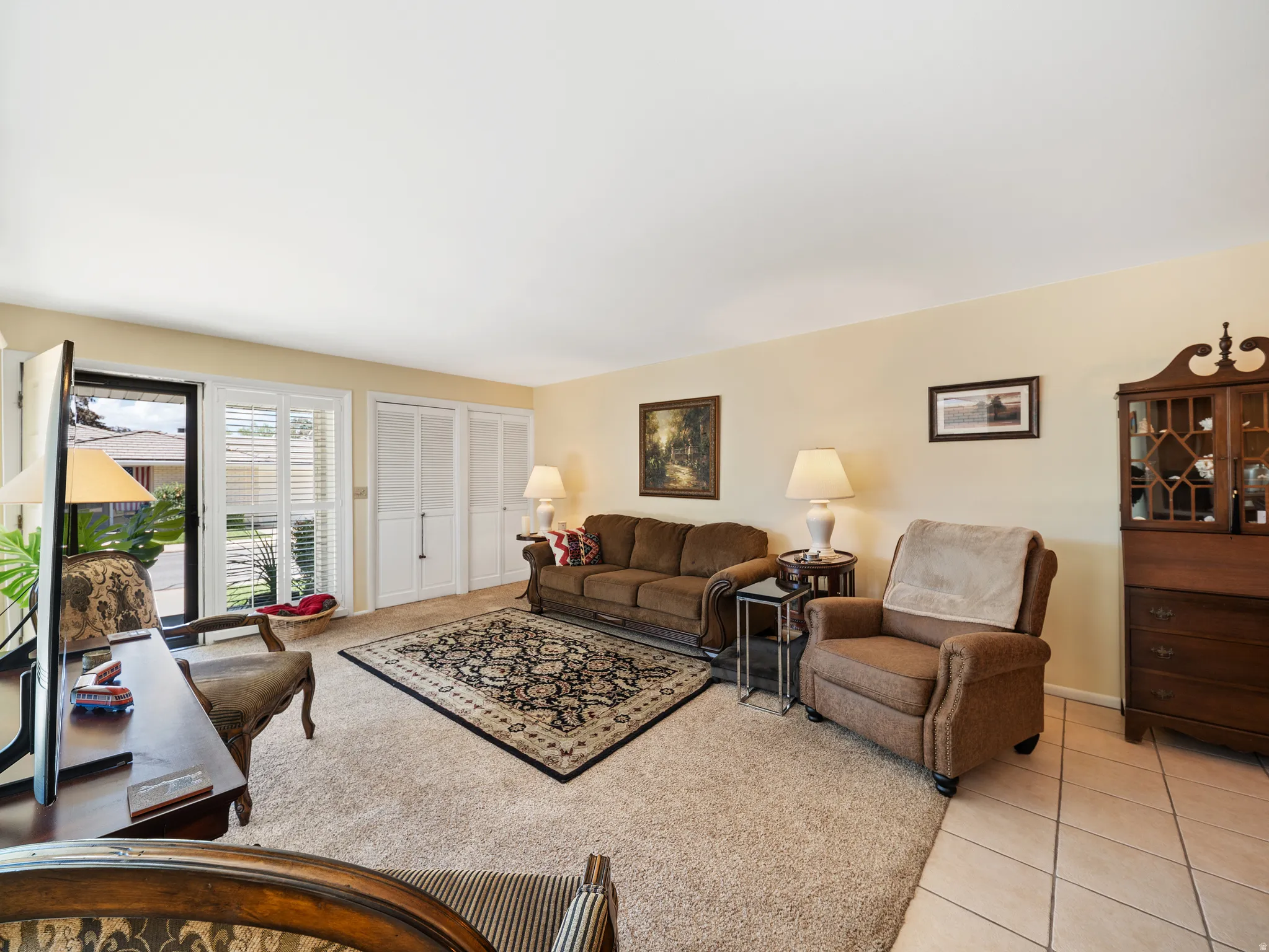 Spacious living room with warm yellow walls, tile flooring, and multiple windows providing natural light
