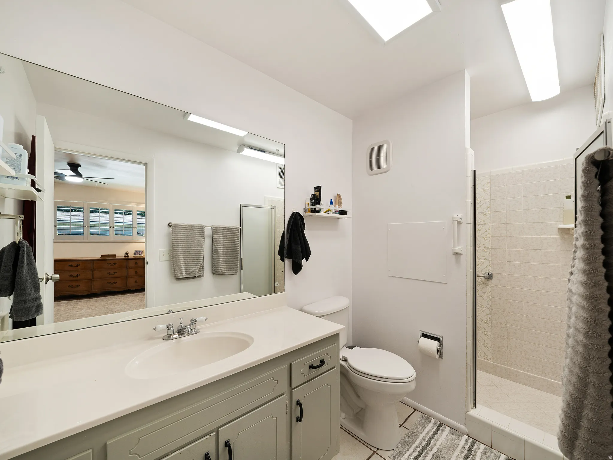 Bathroom with a single vanity, a large wall-mounted mirror, a tiled shower enclosure, and overhead lighting