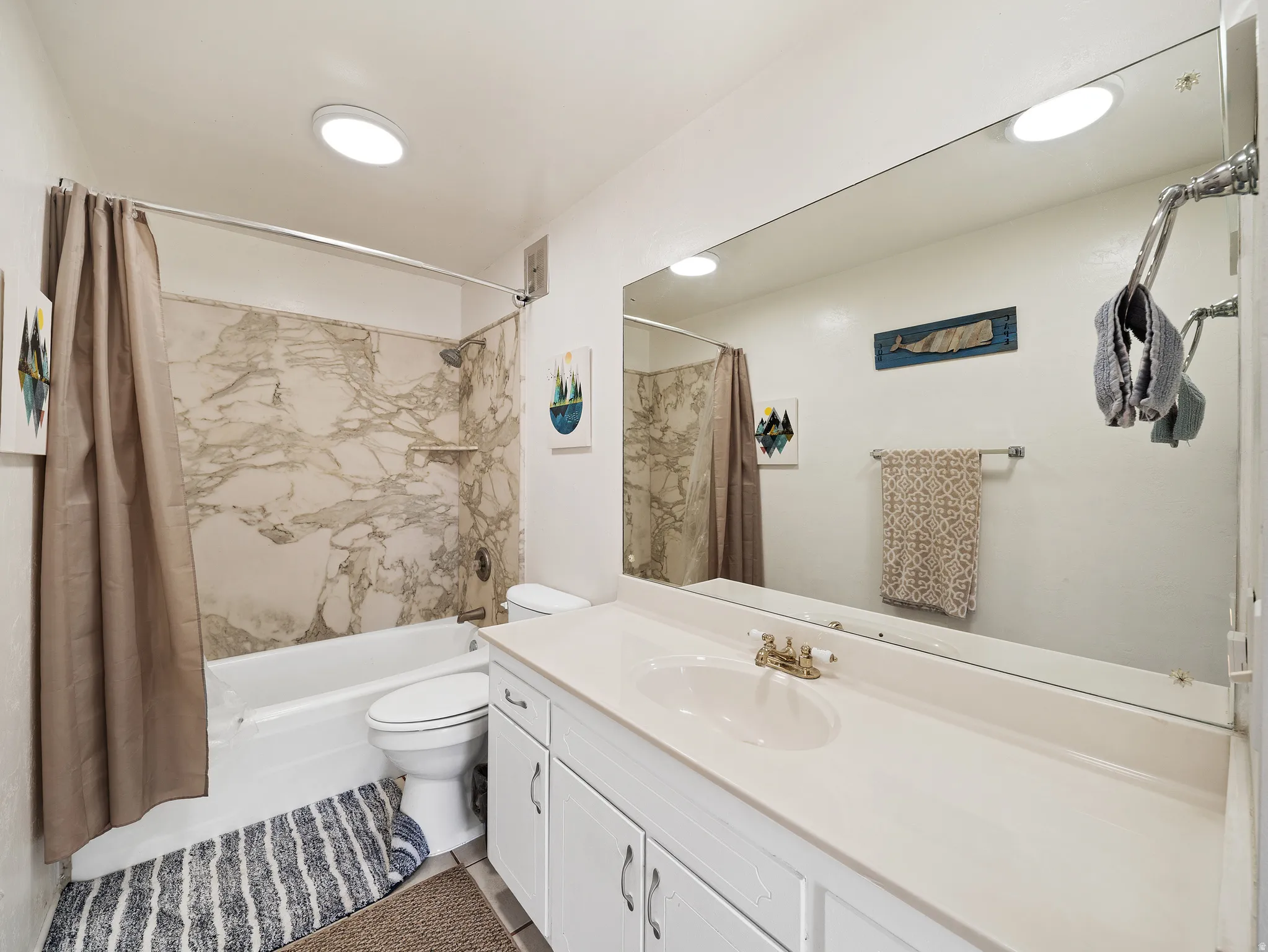 White vanity with cabinetry and an integrated sink, large wall-mounted mirror, and a bathtub with a shower featuring a marbled surround