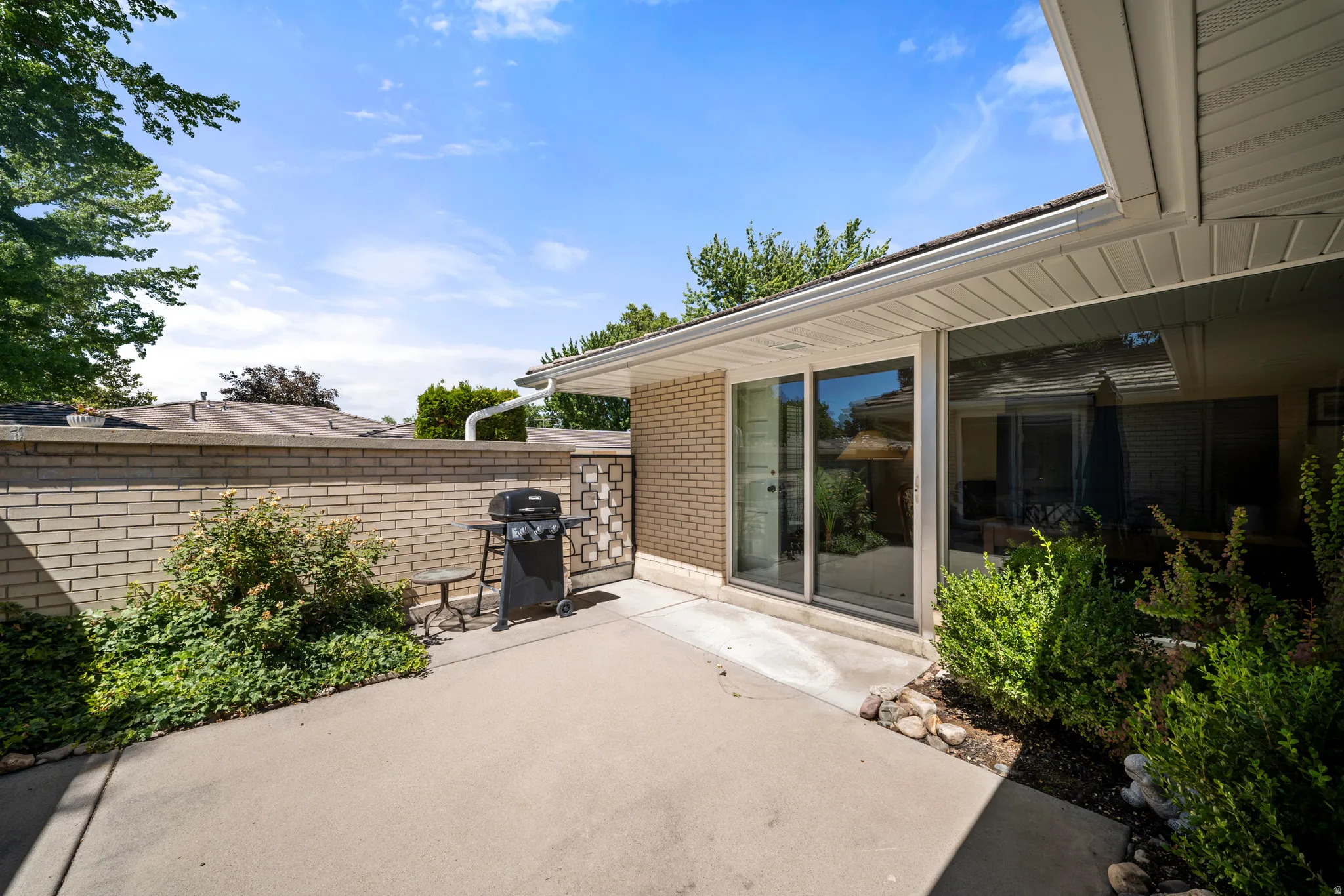 Concrete patio with a brick privacy wall, mature landscaping, and an overhang
