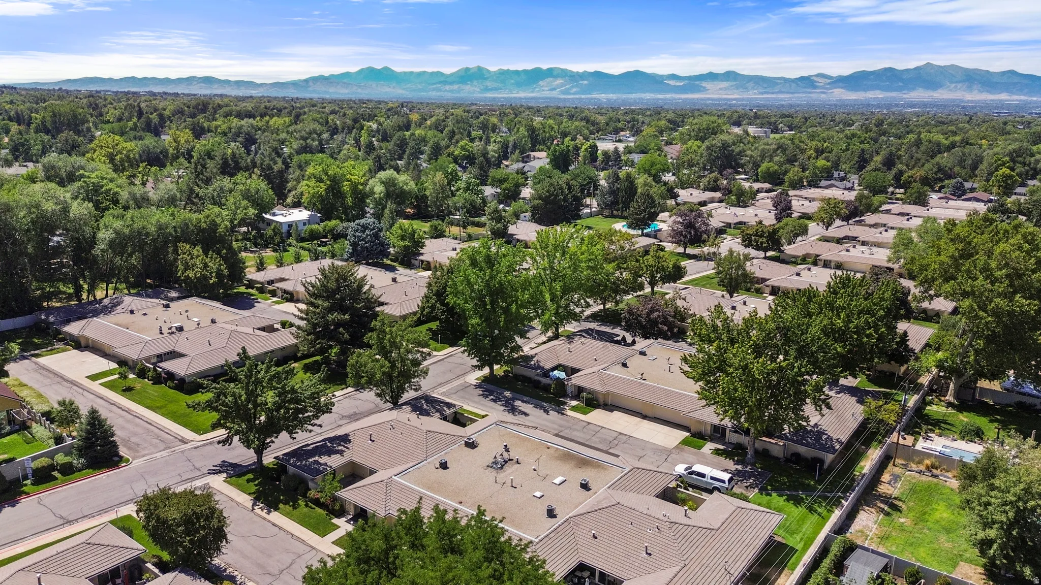 Expansive residential area featuring numerous mature trees, a clear blue sky, and distant mountain ranges