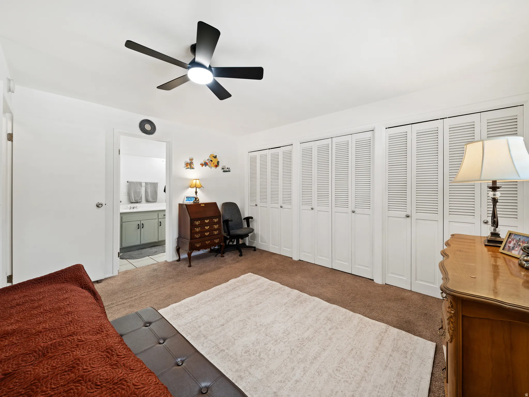 Spacious primary bedroom showcasing hardwood flooring, a ceiling fan with integrated lighting, and extensive closet storage with louvered bifold doors
