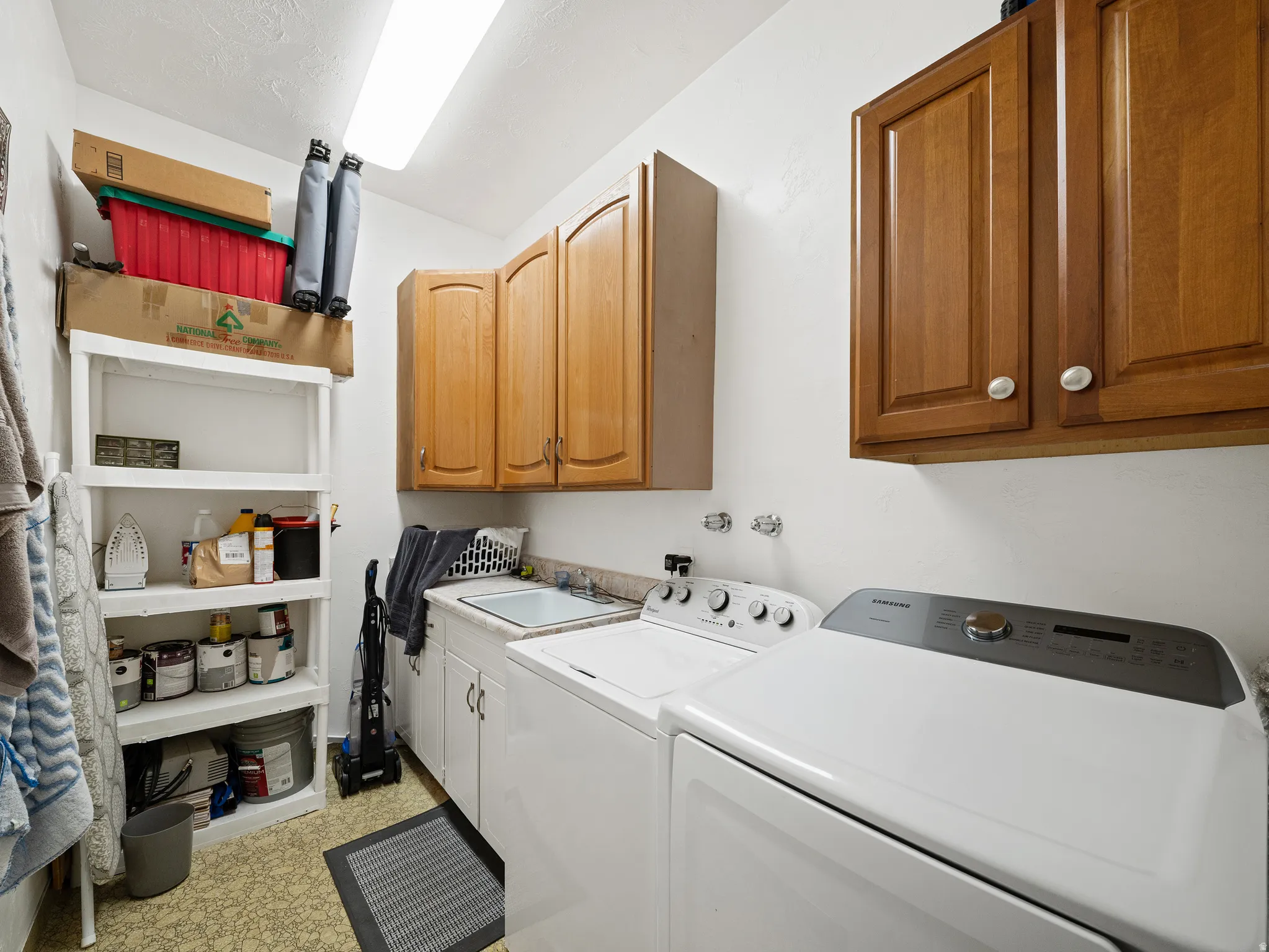 Utility room featuring upper wood cabinetry, white base cabinetry, integrated sink, and patterned flooring