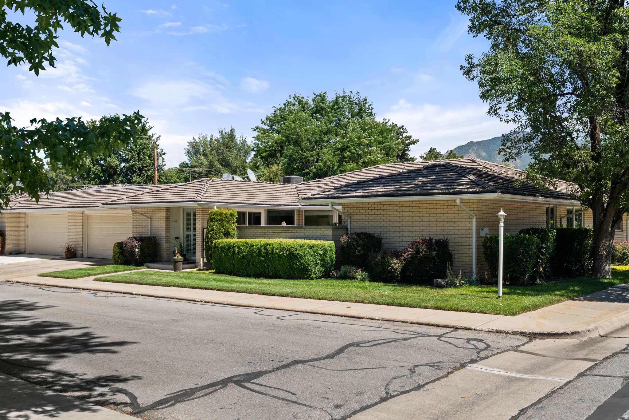 Brick exterior with a tiled roof, mature landscaping, and an attached two-car garage