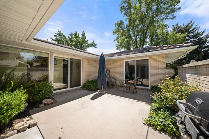 Concrete patio with a brick exterior, multiple large windows, and a shingle roof