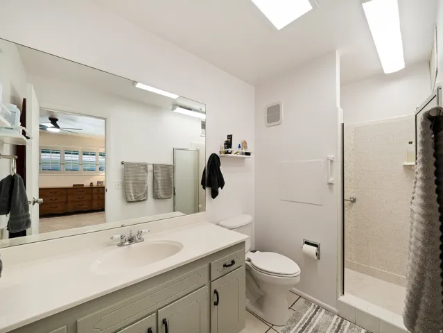 Bathroom with a single vanity, a large wall-mounted mirror, a tiled shower enclosure, and overhead lighting