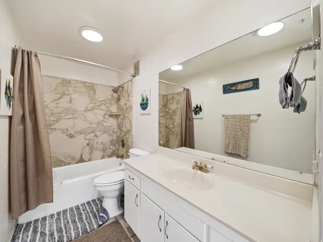 White vanity with cabinetry and an integrated sink, large wall-mounted mirror, and a bathtub with a shower featuring a marbled surround
