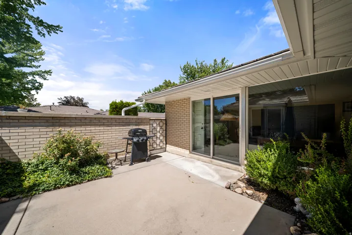 Concrete patio with a brick privacy wall, mature landscaping, and an overhang