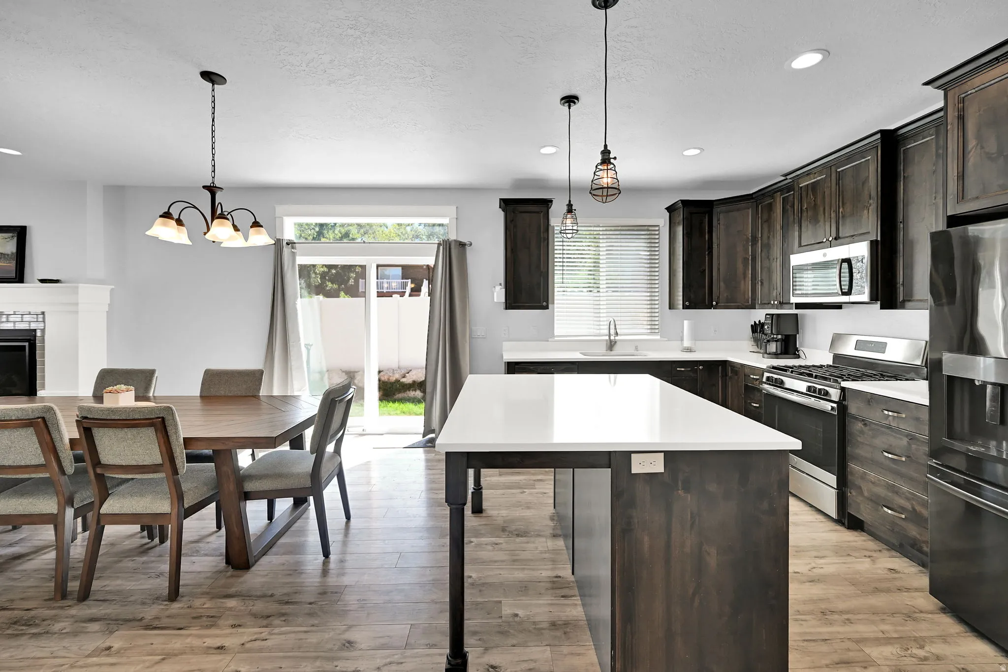 Open-concept kitchen and dining area featuring wood-finish flooring, dark wood cabinetry, white countertops, and stainless steel appliances