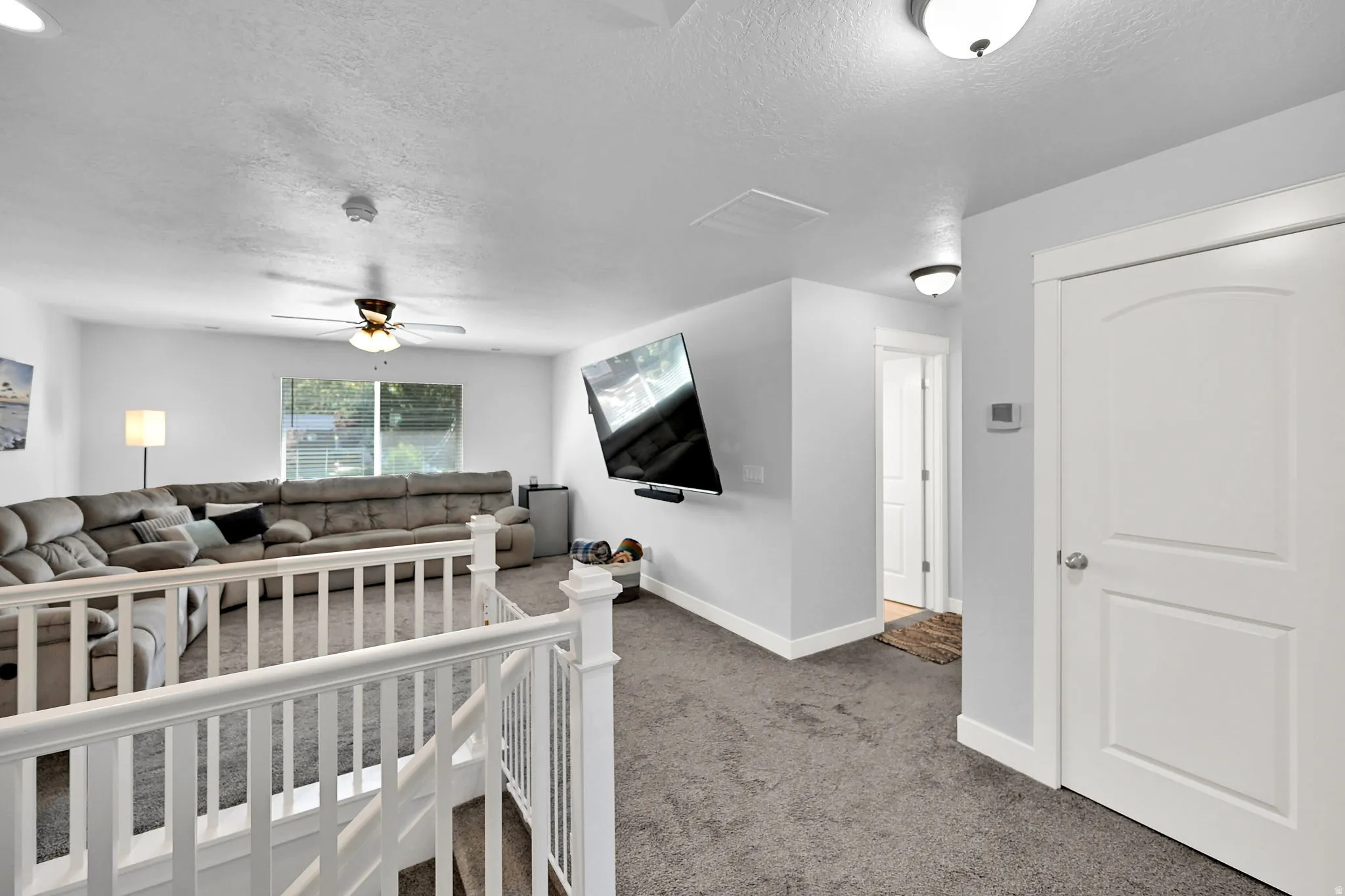 Carpeted living area featuring a ceiling fan, white railings, and a window