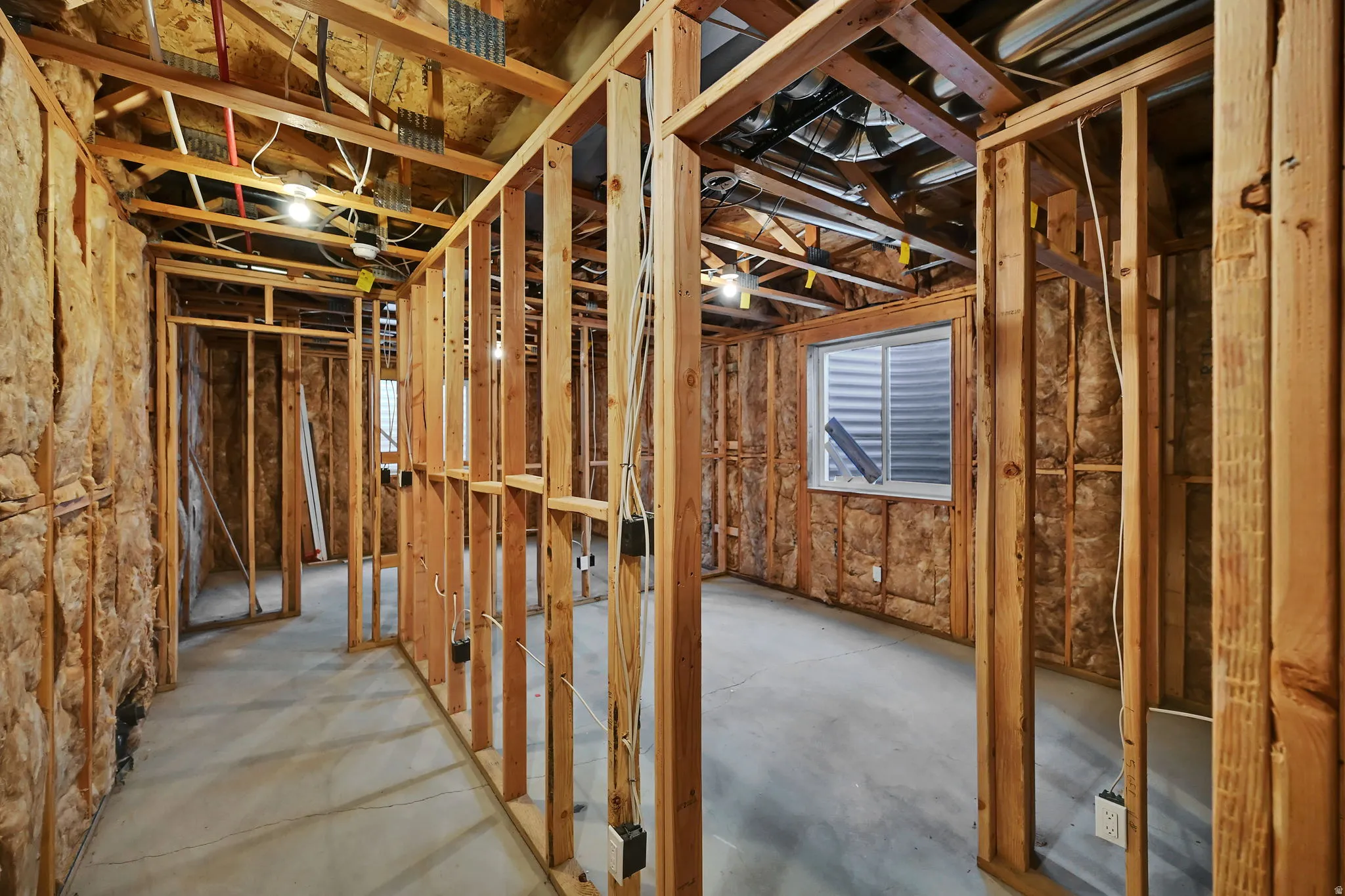 Unfinished basement featuring wood framing, exposed insulation, a concrete floor, and an egress window