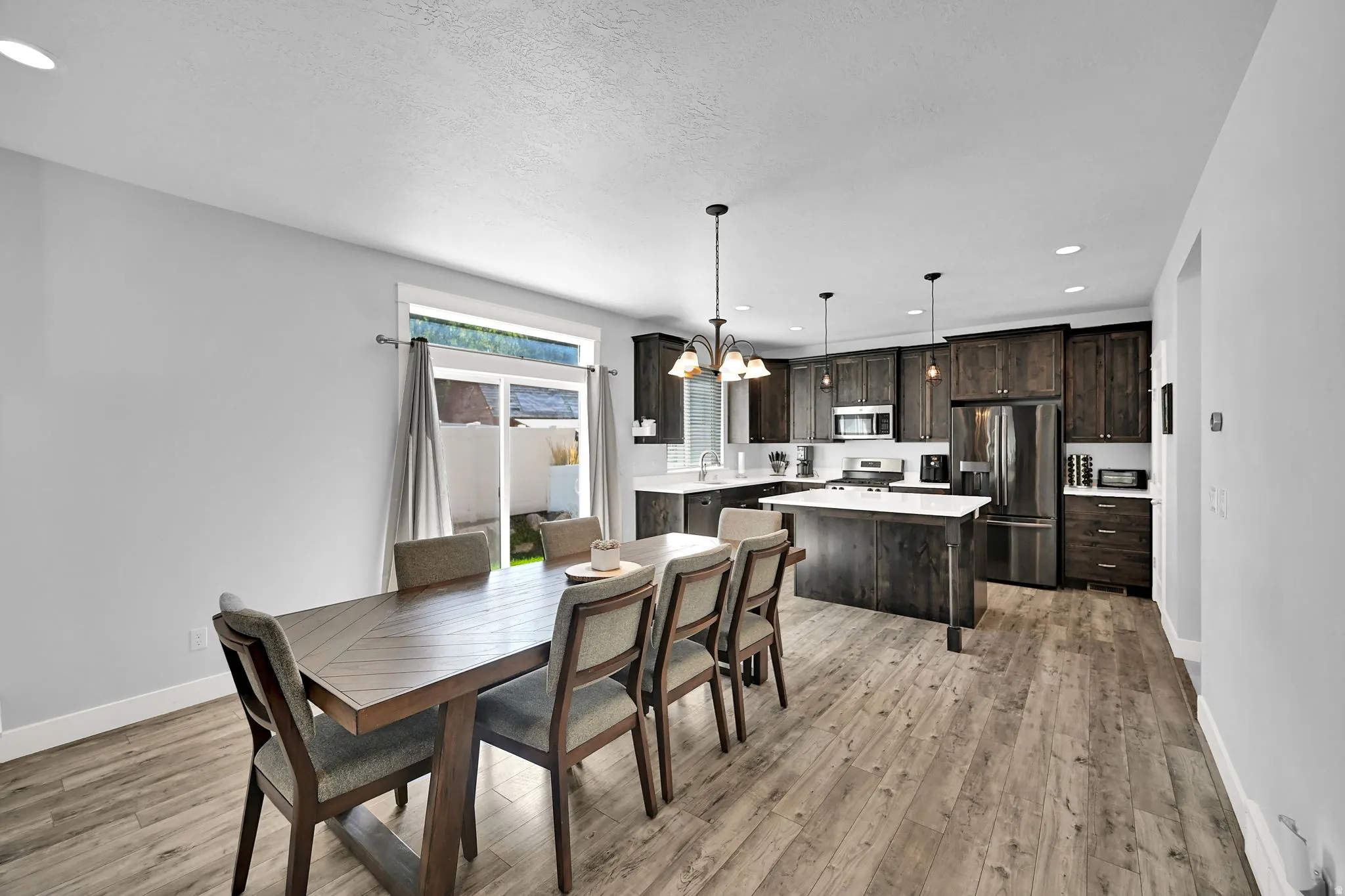Open-concept dining area and kitchen featuring wood-finish flooring, dark wood cabinetry, white countertops, and stainless steel appliances