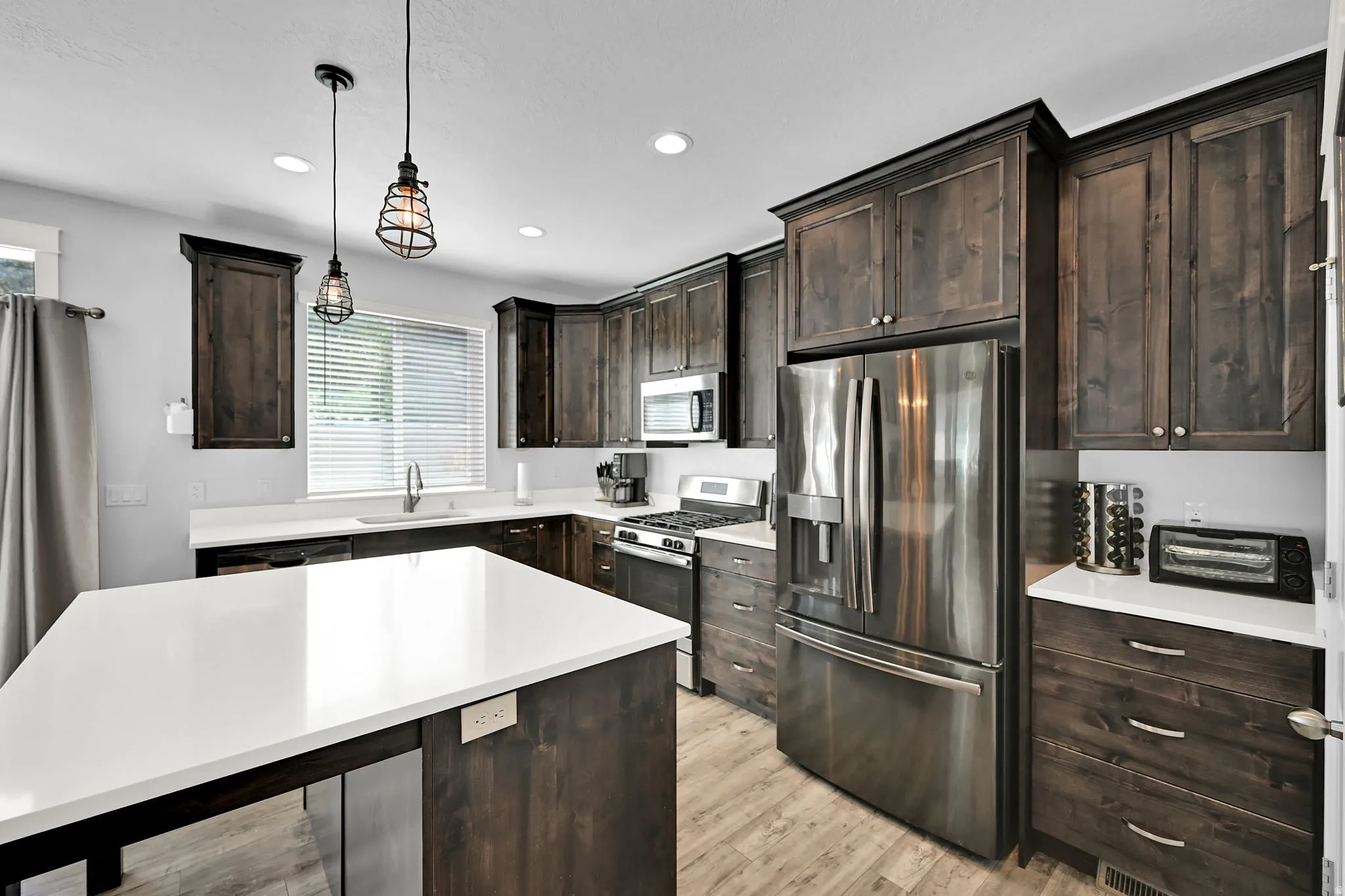 Kitchen featuring dark wood-finish cabinetry, stainless steel appliances, a center island with white countertops, and recessed lighting