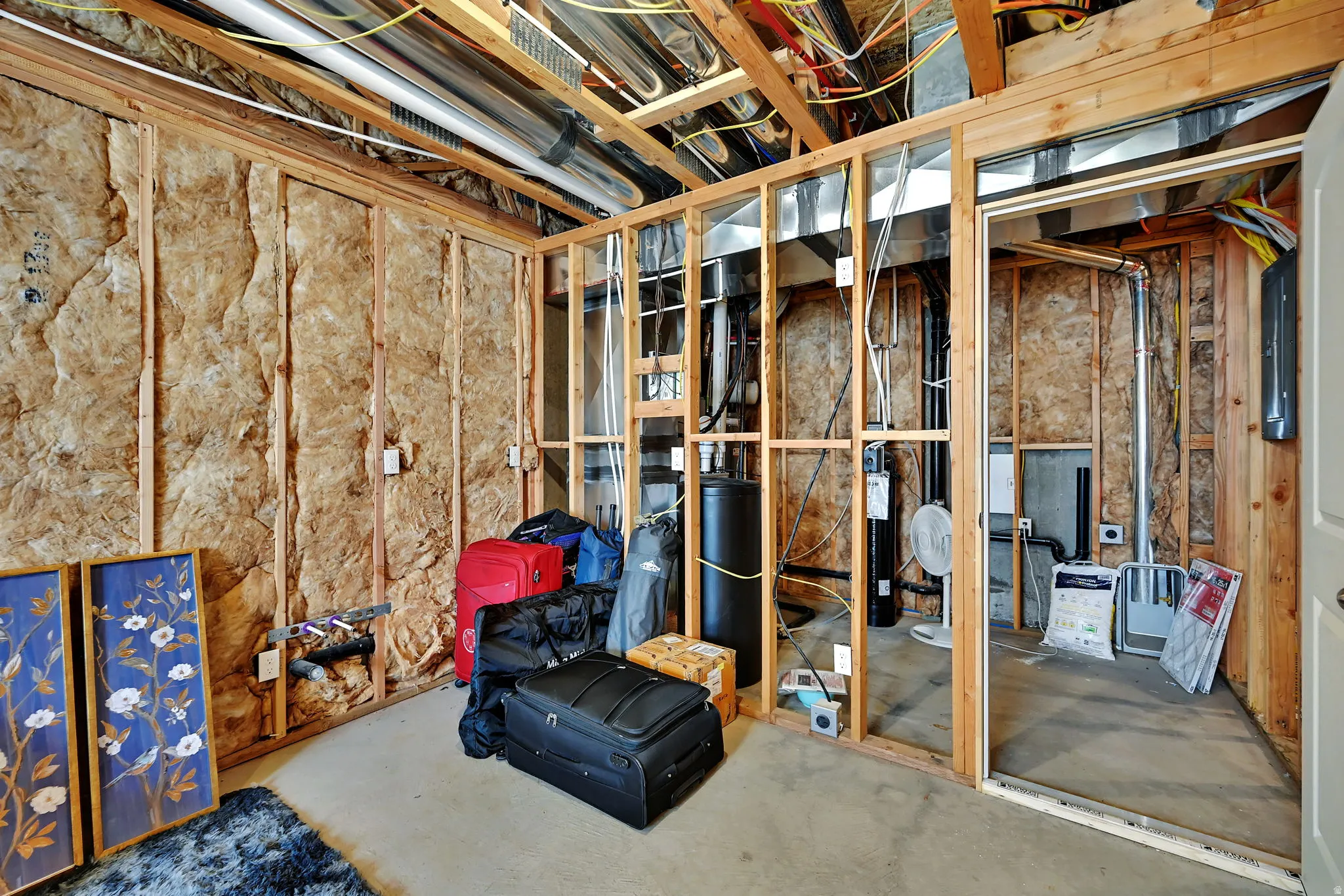 Exposed framing and insulation in an unfinished basement with concrete flooring and visible ductwork