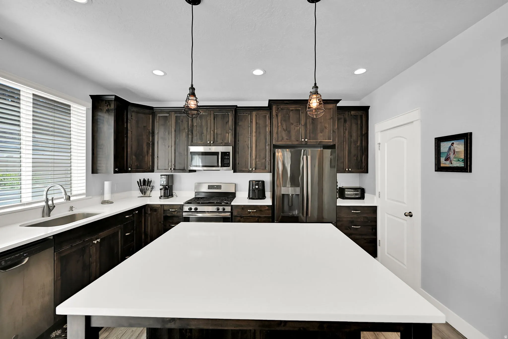 Dark wood-finish cabinetry, stainless steel appliances, white countertops, and a center island with pendant lighting