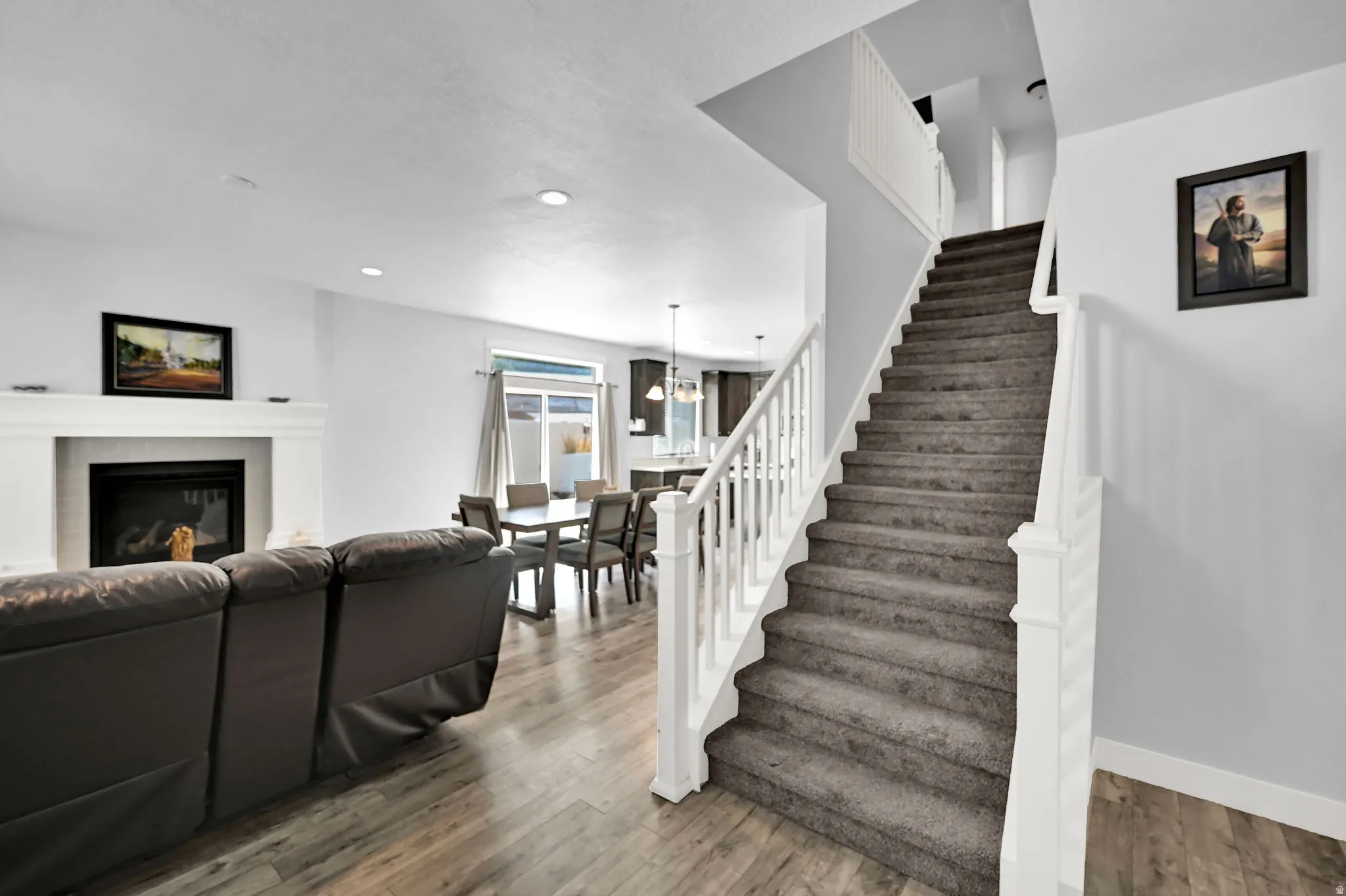 Wood-finish flooring, white fireplace with mantle, sliding glass door, recessed lighting, and carpeted staircase with white banister