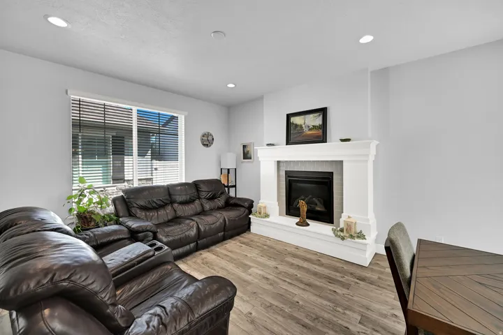 Recessed ceiling lighting, wood-finish flooring, a contemporary fireplace with a decorative mantel, and a large window with horizontal blinds