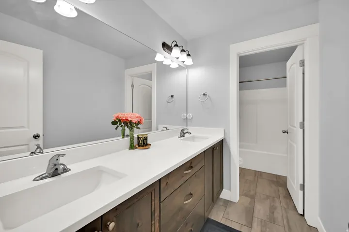 Dual vanity with integrated sinks, wood-finish cabinetry, a large wall-mounted mirror, and tile flooring