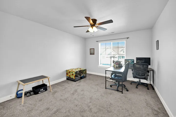 Carpeted room with a ceiling fan light fixture and a window featuring blinds