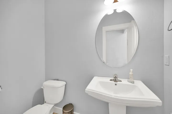Pedestal sink with chrome faucet, oval mirror, and wall-mounted light fixture