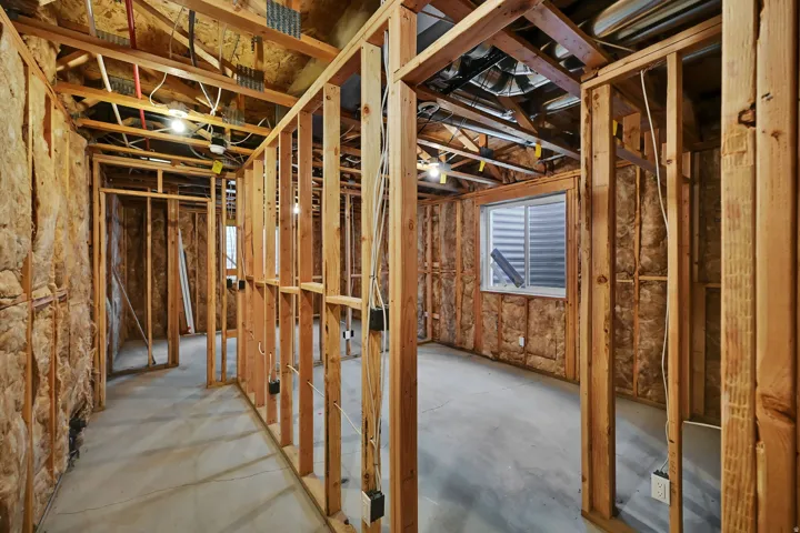 Unfinished basement featuring wood framing, exposed insulation, a concrete floor, and an egress window