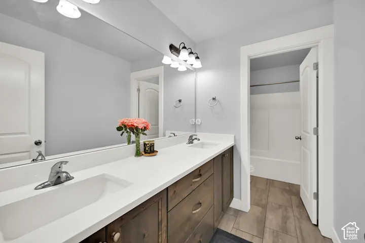 Dual vanity with integrated sinks, wood-finish cabinetry, a large wall-mounted mirror, and tile flooring
