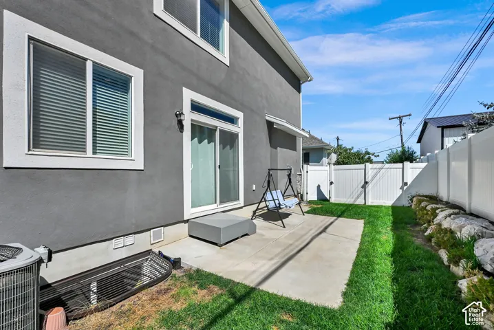 Private patio with direct access via sliding glass doors, surrounded by green space, and secured by a white privacy fence