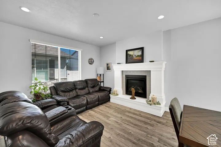 Recessed ceiling lighting, wood-finish flooring, a contemporary fireplace with a decorative mantel, and a large window with horizontal blinds