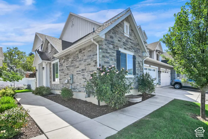 Stone veneer exterior with gabled roofline, multiple windows with dark shutters, and an attached two-car garage