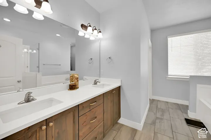 Dual undermount sinks with chrome fixtures, wood-finish cabinetry, a large vanity mirror, and tile flooring