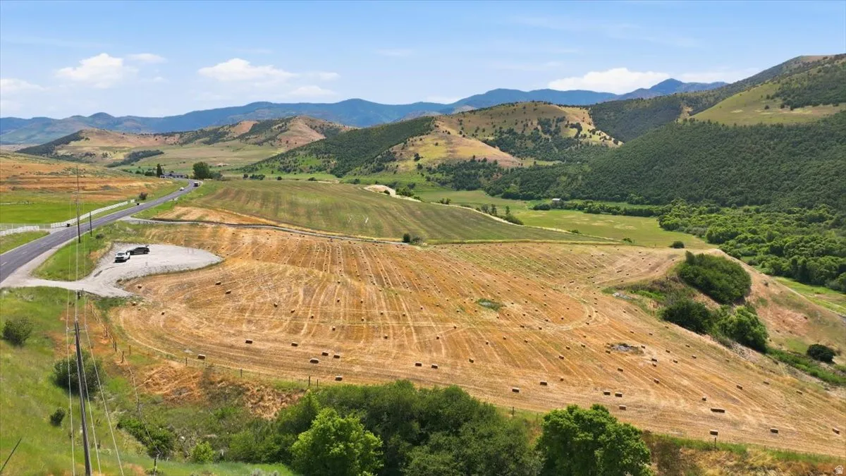 Expansive open land featuring a paved roadway, mountainous terrain, and agricultural fields