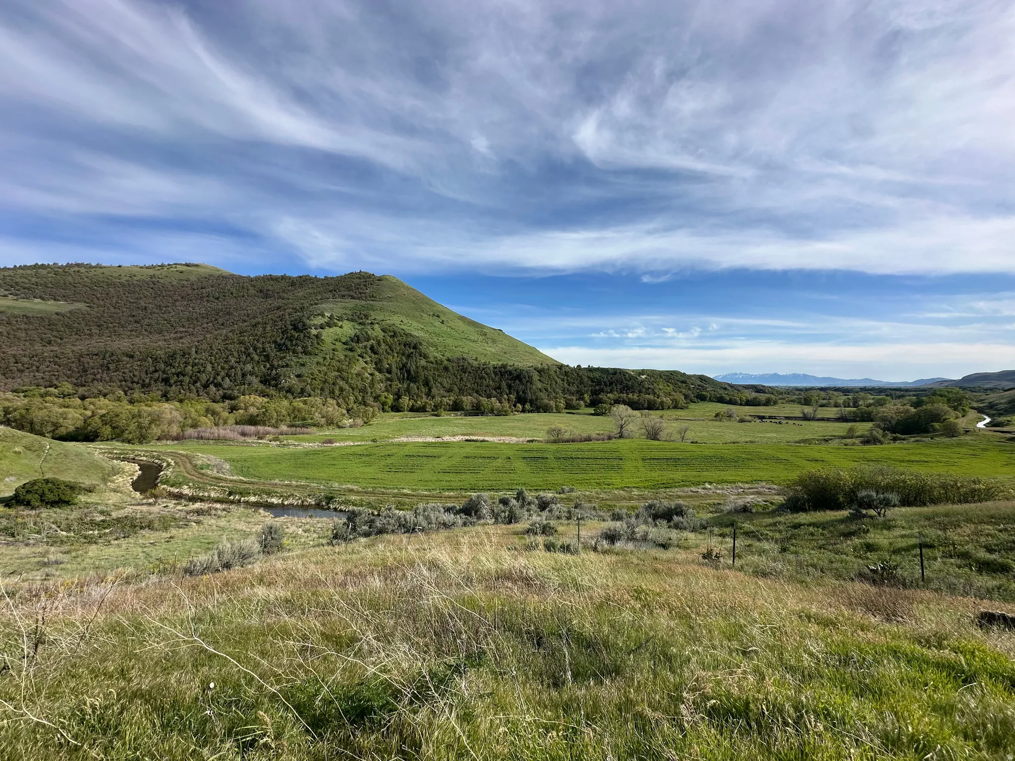 Expansive land featuring rolling hills, a meandering stream, and distant mountain ranges