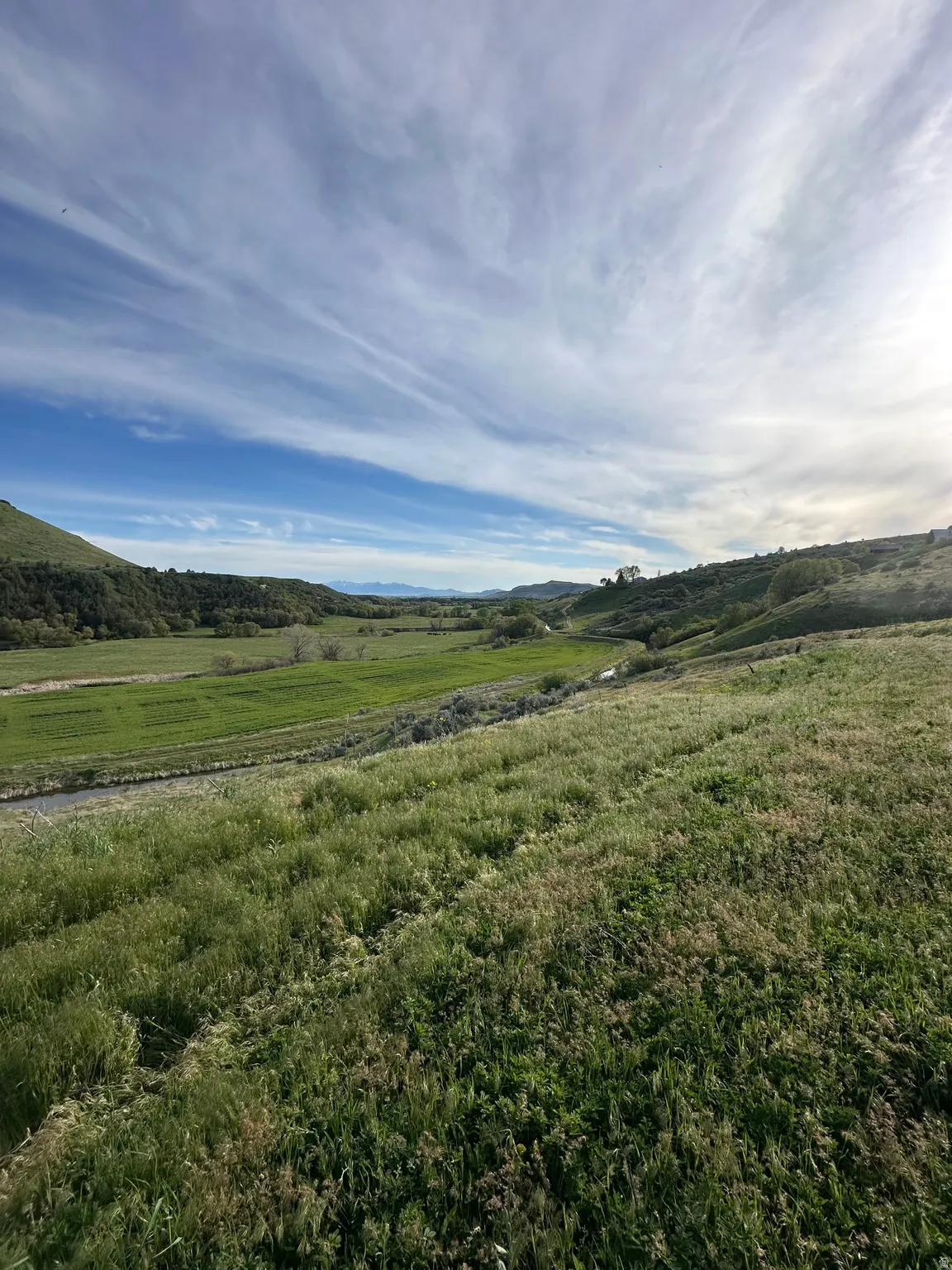 Expansive land parcel featuring open fields, rolling hills, natural waterways, and distant mountain ranges