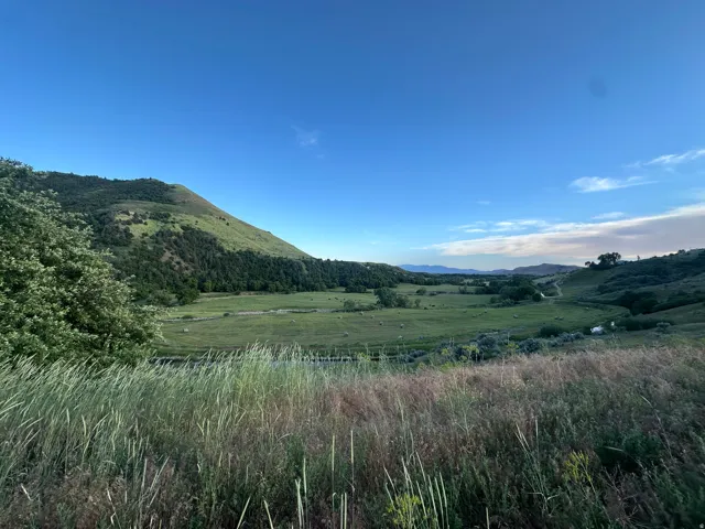 Expansive natural landscape with rolling hills, lush green fields, and distant mountains