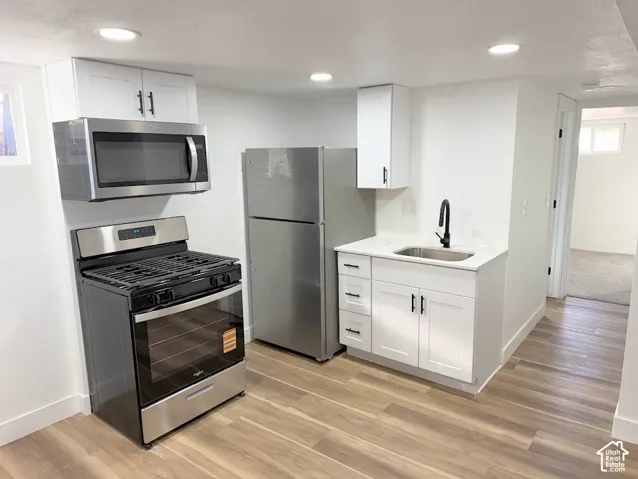 Kitchen featuring white shaker-style cabinetry, stainless steel appliances, matte black hardware, recessed lighting, and wood-finish flooring