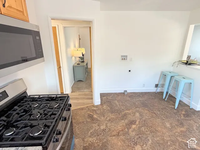 Stainless steel range with a gas cooktop, overhead microwave, and wood-finish cabinetry